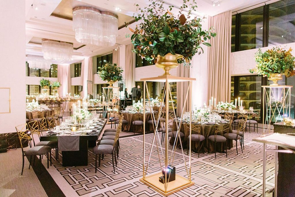 Very large gold, modern pedestal with florals placed throughout the wedding reception room.